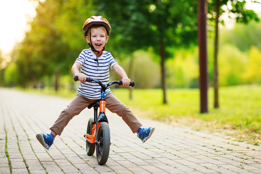 Employee Benefits - Happy Child Rides His Bike on a Sidewalk in the Park in Summer on a Sunny Day