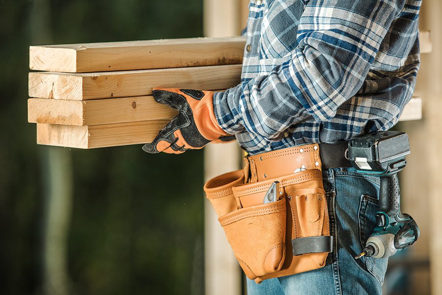 Specialized Business Insurance - Closeup of Contractor Holding Wooden Beams While Standing in Front of Blurred Construction Area of a Home